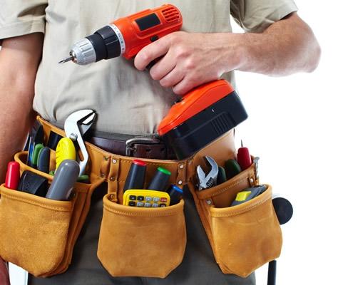 Muž drží vrtačku a má na opasku nářadí pro opravy